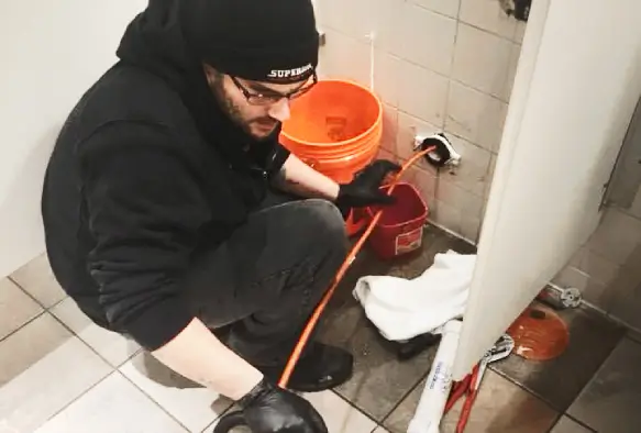 Plumber repairing sewer line with drain snake and bucket, Superior Sewer & Drain Service.