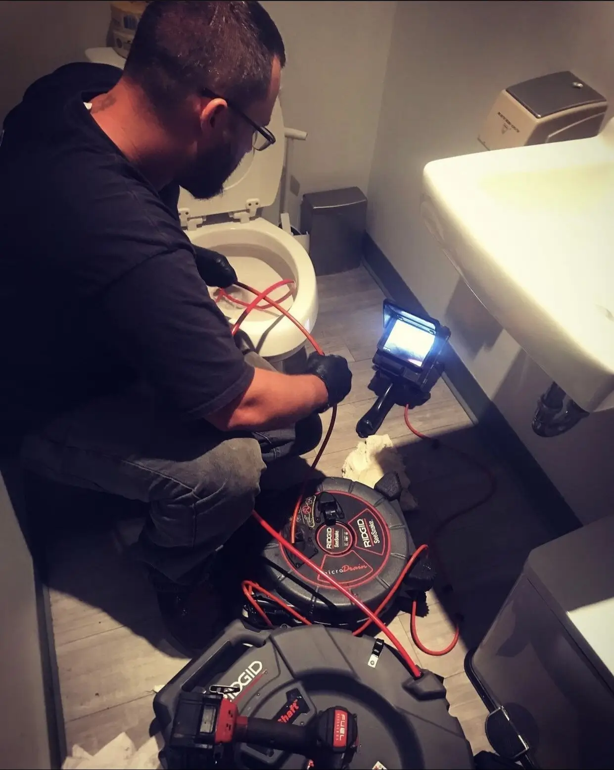 Plumber using camera inspection equipment to diagnose clogged toilet and sink.